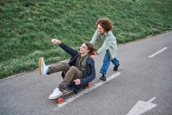 Happy teenager girl pushing laughing friend on skateboard. Friends having fun on a skateboard during spring or summer break time.