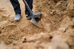 A man is standing on a pile of sand and digging with a steel shovel.