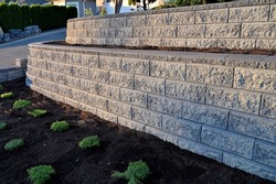 A beautiful view of a gray colored 2 tier retaining wall built with concrete blocks in early morning sunlight.