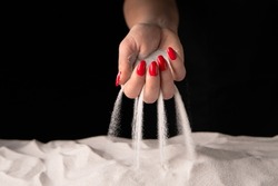 Woman with handful of white dry sand in her hands, spilling sand through fingers on black studio background. Concept of flow of life. Close up of grains of pure natural mineral quartz in female hand.