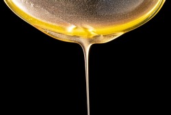 Honey dripping, pouring thick jet on black background. Viscous yellow honey molasses flowing. Close up of golden honey liquid, sweet product of beekeeping. Sugar syrup is pouring flow.