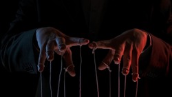 Male hand with marionette strings on black isolated backgorund. Boss in a black business suit controlling managers. Concept of dictatorship and control of the government of the people. Close up.