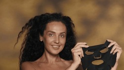 A woman holds a black cosmetic sheet mask. Seminude woman in the studio on a yellow background with highlights. The concept of beauty, cosmetology, care.