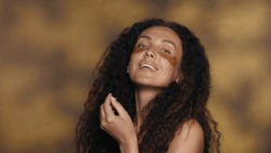Longhaired curly brunette woman performs cosmetic procedures. Portrait of a seminude woman with golden patches under her eyes in the studio on a yellow background with highlights close up.
