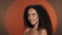 Portrait of a seminude woman with regular features and perfect skin close up. Curly woman in the studio on an orange background with circular light. Facebuilding.