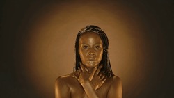 Portrait of a seminude woman with golden skinon a brown background with circular light. The woman wraps her arms around her neck. Fashion, art, design, cosmetology.
