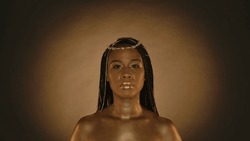 Portrait of a seminude African American woman in the style of Cleopatra in the studio on a brown background with circular light. A woman with creative golden makeup, golden skin, jewelry in her hair.