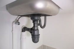 Pipe under kitchen sink. Consist of stainless steel, concrete counter, pvc plastic pipe, faucet, trap. Part of drainage and plumbing system. For water or sewer drain, siphon, repair and maintenance.