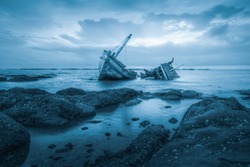 Shipwreck or wood ship broken damage on land, coast or beach with sea and sunset background. That result of accident, storm, crash, wave in ocean or marine. For assurance, travel or adventure concept.