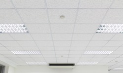 Office ceiling in perspective with white texture of acoustic gypsum plasterboard, lighting fixtures or fluorescent panel light suspended on square grid structure. Interior modern building background.
