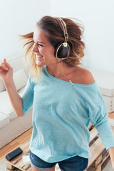 Happy girl dancing at home while listen music with headphones. She is in her home