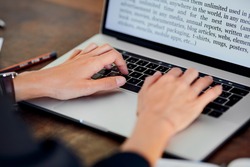 Stock photo of female hands touching keyboard of laptop with words on screen. Crop office worker typing document using modern gadget. Concept of business
