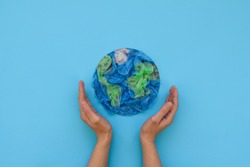 Hands holding planet Earth made from plastic disposable packages on blue background. Save the world, creative, environment pollution or World Earth Day concept. Top view