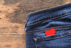 Small red heart in jeans pocket on wooden table