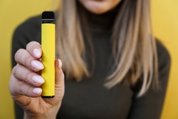 Yellow disposable electronic cigarette in female hand. Bright yellow background
