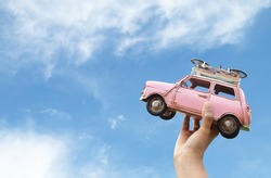 woman hand holding miniature car with blue sky and clouds,(travel concept)