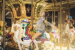 Stylish woman wearing sparkling jacket on the carousel in theme park