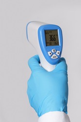 Doctor is holding a digital infrared thermometer on gray background