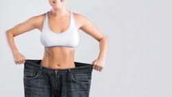 Woman showing result after weight loss wearing on old jeans on gray background