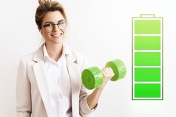 Energized business woman lifting green dumbbell. Fully charged battery symbol beside. Concepts of active life, stress free work and uplifting.