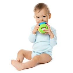 Adorable little boy in a romper is sitting and playing with plastic toy, putting it in his mouth on white background.