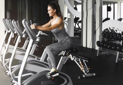 Young cheerful woman is cycling on stationary bike during her cardio workout in the modern gym