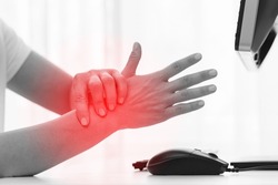 Young woman working in office with a carpal tunnel syndrome or wrist joint inflammation
