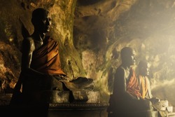 Closeup shot of metallic buddhist monk statues inside a dark cave in Thailand.