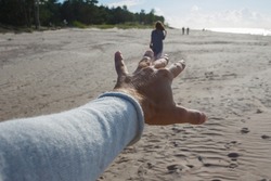 Point of view shot of a man reaching hand and chasing a leaving woman after a break up at sandy sea shore.