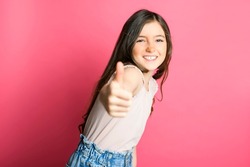 A cute positive thumb up child over pink backgroud on studio
