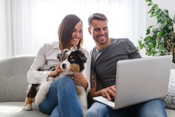 A Handsome couple with her Australian Berger puppy on sofa with laptop