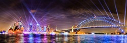 WIde panorama of Sydney city CBD landmarks and high-rise office buildings on waterfront of Harbour with the Sydney harbour bridge at Vivid Sydney light show illumination.