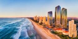 Rising sun shining on modern urban towers of Surfers paradise in Australian Gold Coast facing endless waves of Pacific ocean - aerial panoramic view.
