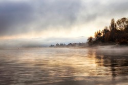 Yellow autumnal park on shores of Lake Jindabyne on Snowy River in Australia - golden hour sunrise with mist, fog and reflecting sun light.