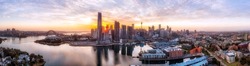 WIde aerial panorma at sunrise over CIty of Sydney with towers hiding the rising sun on shores of Sydney harbour and major architecture landmarks.