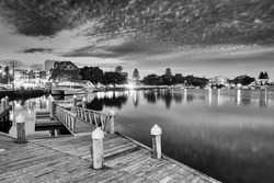 Contrast black-white wooden boardwalk along Coolongolook river Wallis lake in Forster town of Australia at sunset around harbor boat berths.