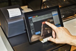 POS terminal in coffee cafe waiter's hand when serving customers and touching screen of a tablet with software interface to take order and print receipt.
