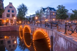 Netherlands. Stone bridge with three arches on the Amsterdam Canal. Lots of parked bikes. A few minutes before dawn