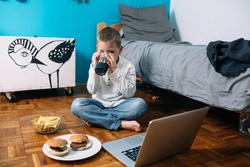 young boy playing games on laptop computer and eating jung food.online games addicted