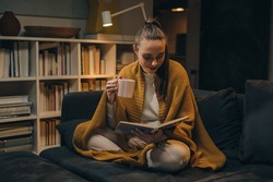 woman reading book and drinking coffee or tea at home