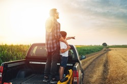 father and son standing on trunk of truck on farmland