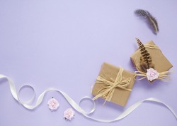 Gift wrap - Presents wrapped in brown parcel paper with raffia bows, pink rose flowers and feathers, on a purple background with white silk ribbon forming a page border