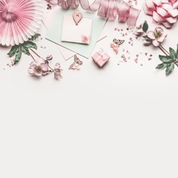 Beautiful pastel pink work space with flowers decoration,ribbon, hearts, bow and card mock up on white desk background, top view, flat lay, border. Wedding invitation or Mother Day greeting concept