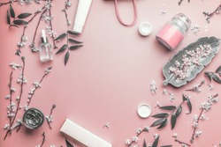 Cosmetic and skin care concept. Various facial cosmetic products on pastel pink background with cherry blossom and leaves, top view, frame. Copy space for your design. Beauty blog layout. Flat lay