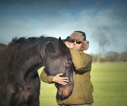 Man in winter hat hugging black old horse