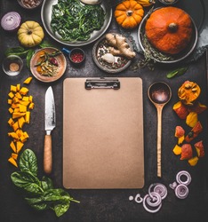 Food background for tasty winter and autumn dishes with pumpkin. Various cooking ingredients with spoon and knife around blank cardboard clipboard for menu or recipes , top view, frame, mock up
