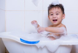 Asian happy funny little children boy shower and playing with water in bathroom and have shampoo foam bubble on white wall at house.
