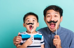 Family funny happy hipster father and his son kid holding black mustache props for the photo booth close face, studio shot isolated on a blue background, men health awareness