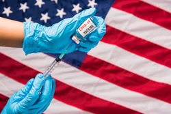 Hands of doctor wear gloves holding coronavirus (COVID-19) vial vaccine and syringe on flag United States of America background, USA Vaccination