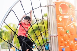 Asian child smiling playing climbing outdoor playground, happy preschool little kid having funny while playing climbs on a rope climbing net on playground equipment in daytime in summer, Little boy